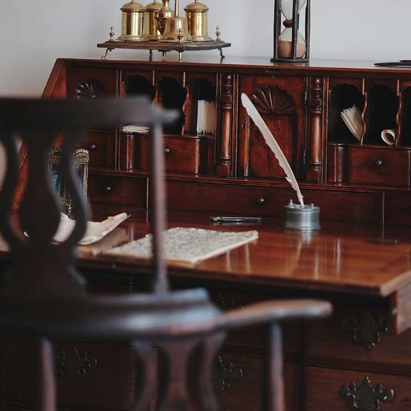 Bureau avec une chaise. Des feuilles de papier sont posées sur le bureau avec un encrier et une plume.